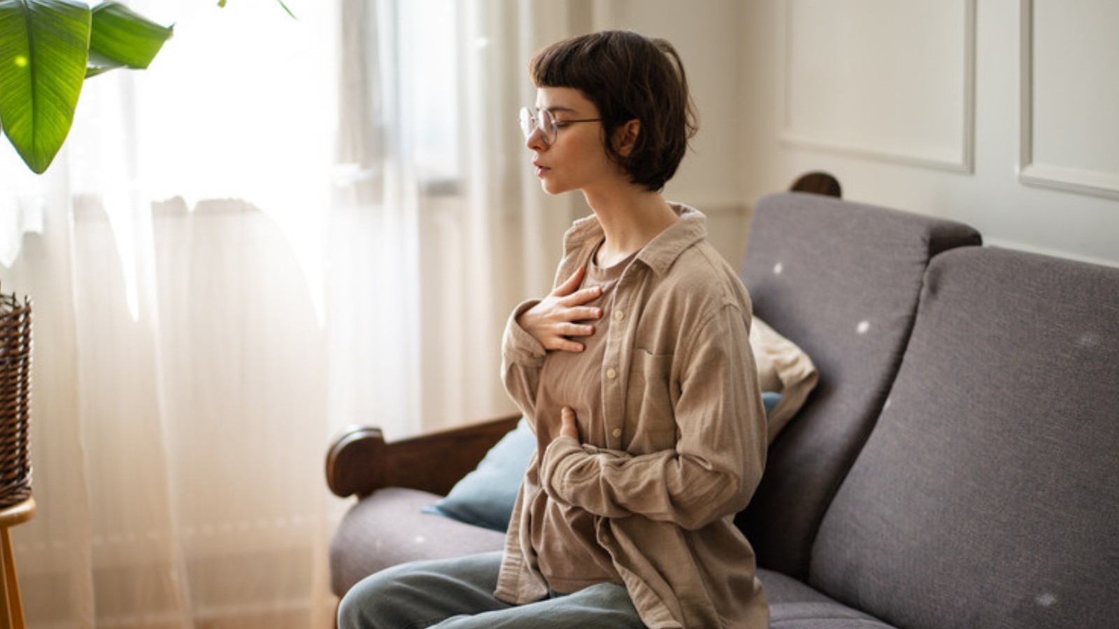 Femme assise sur un canapé, une main sur le cœur, dans un moment de respiration calme