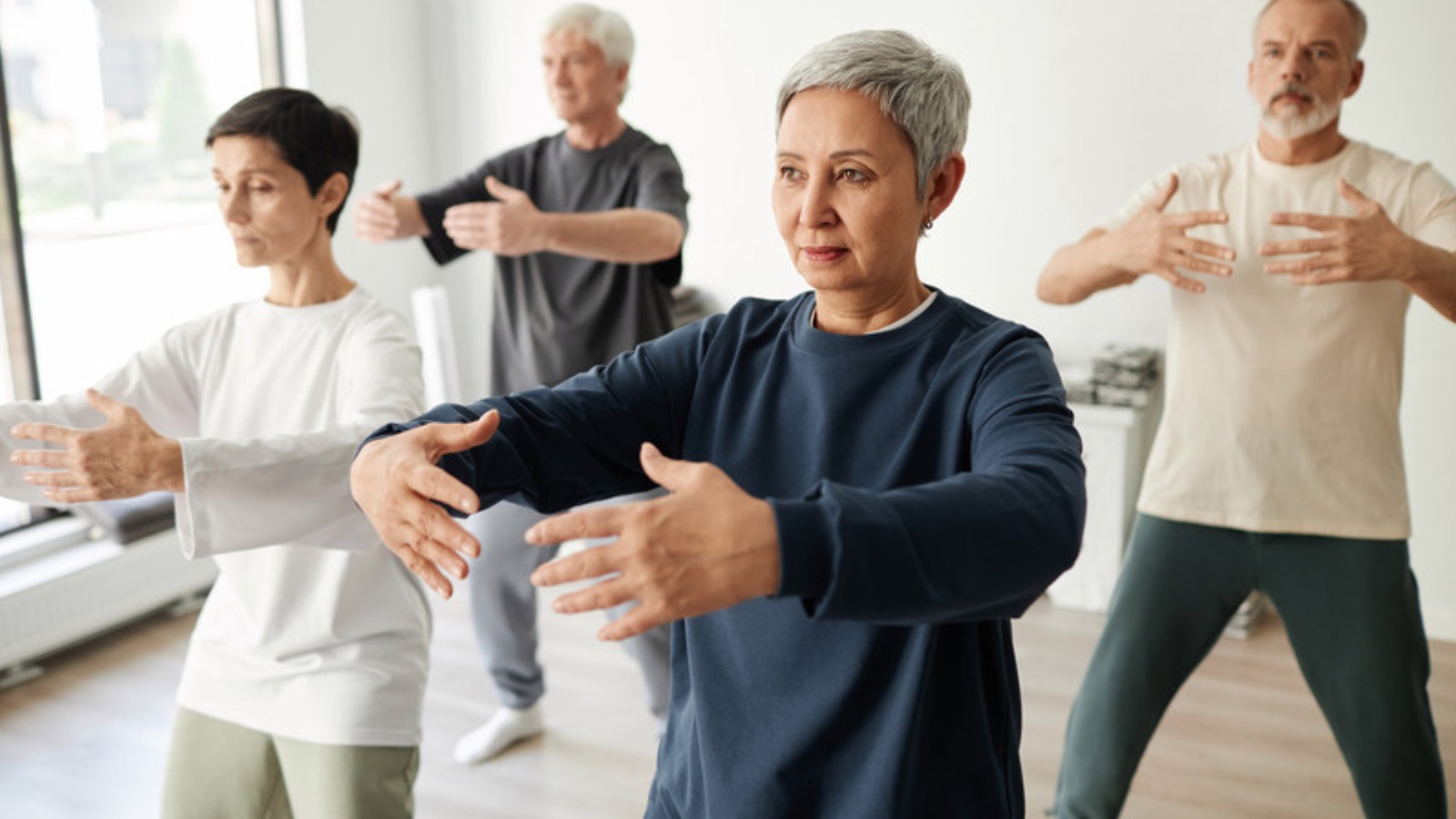 Groupe pratiquant le qigong en studio, bras arrondis en posture de l'arbre