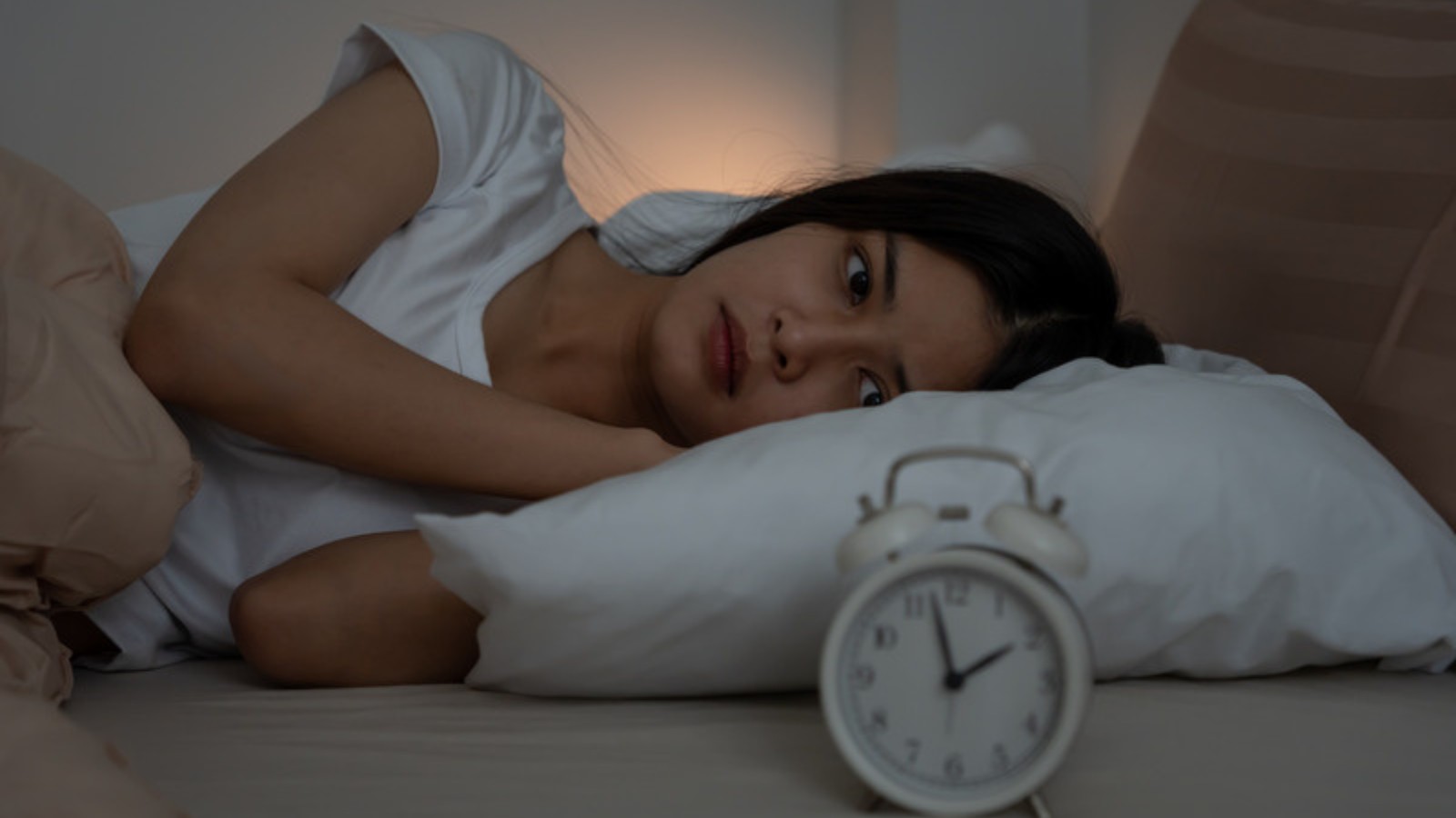 Femme éveillée dans son lit la nuit, réveille-matin indiquant environ 2 h